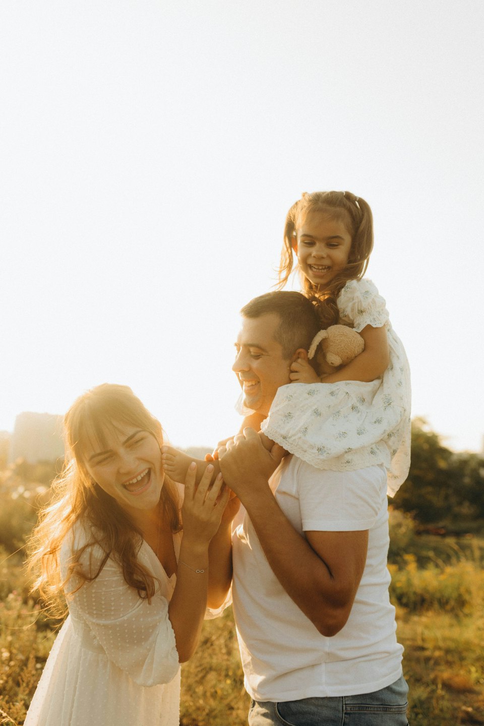 Parents play with their daughter in a grassy field.