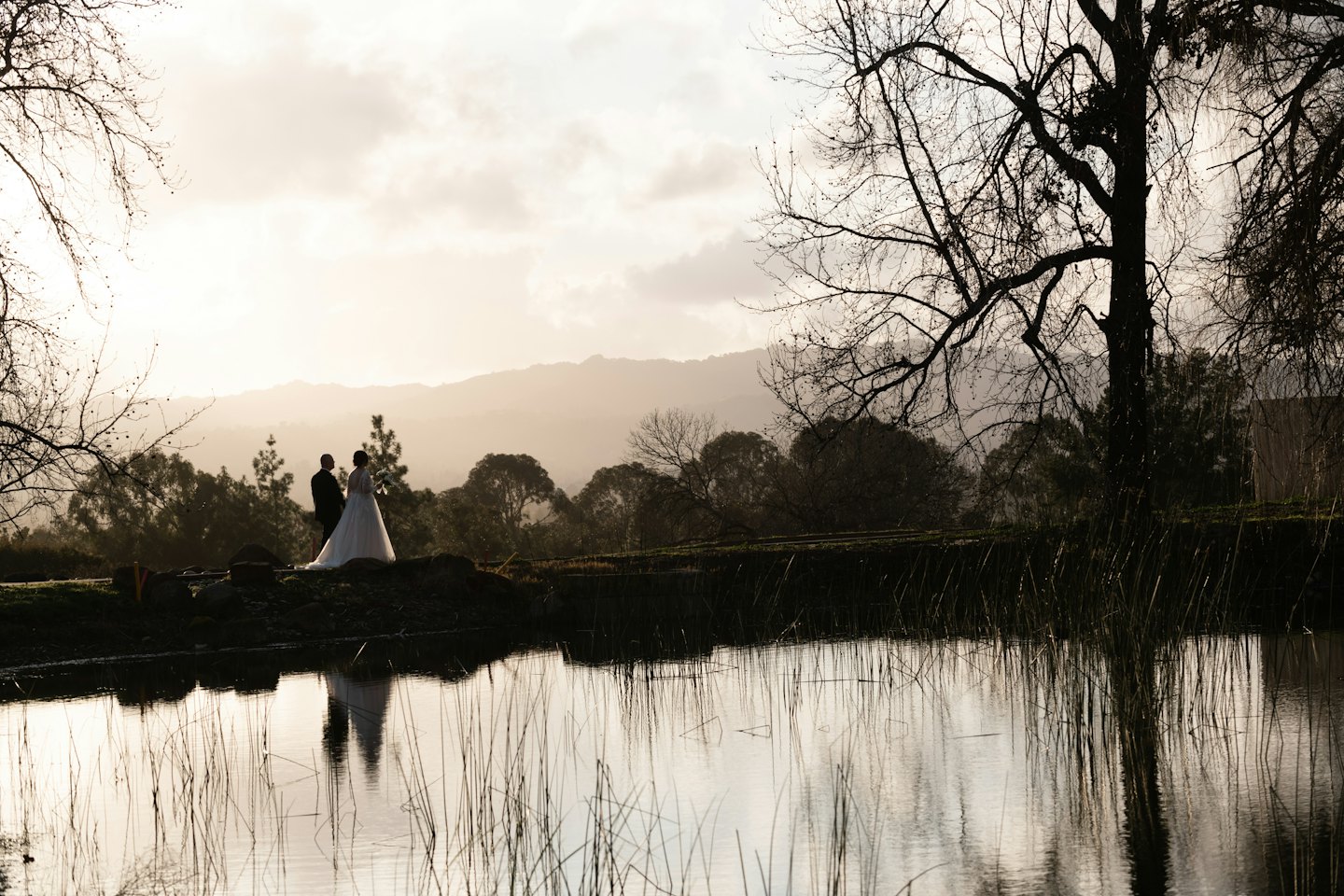 Bride and groom standing beside a reflective lake.