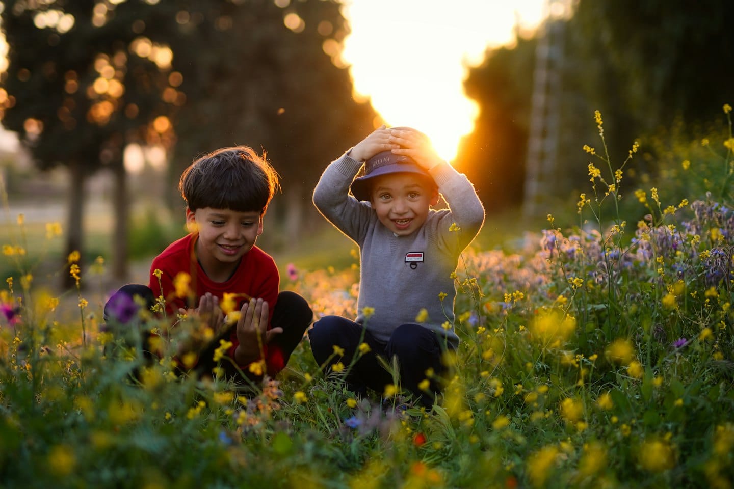 Two boys crouch and play in a field of wildflowers.