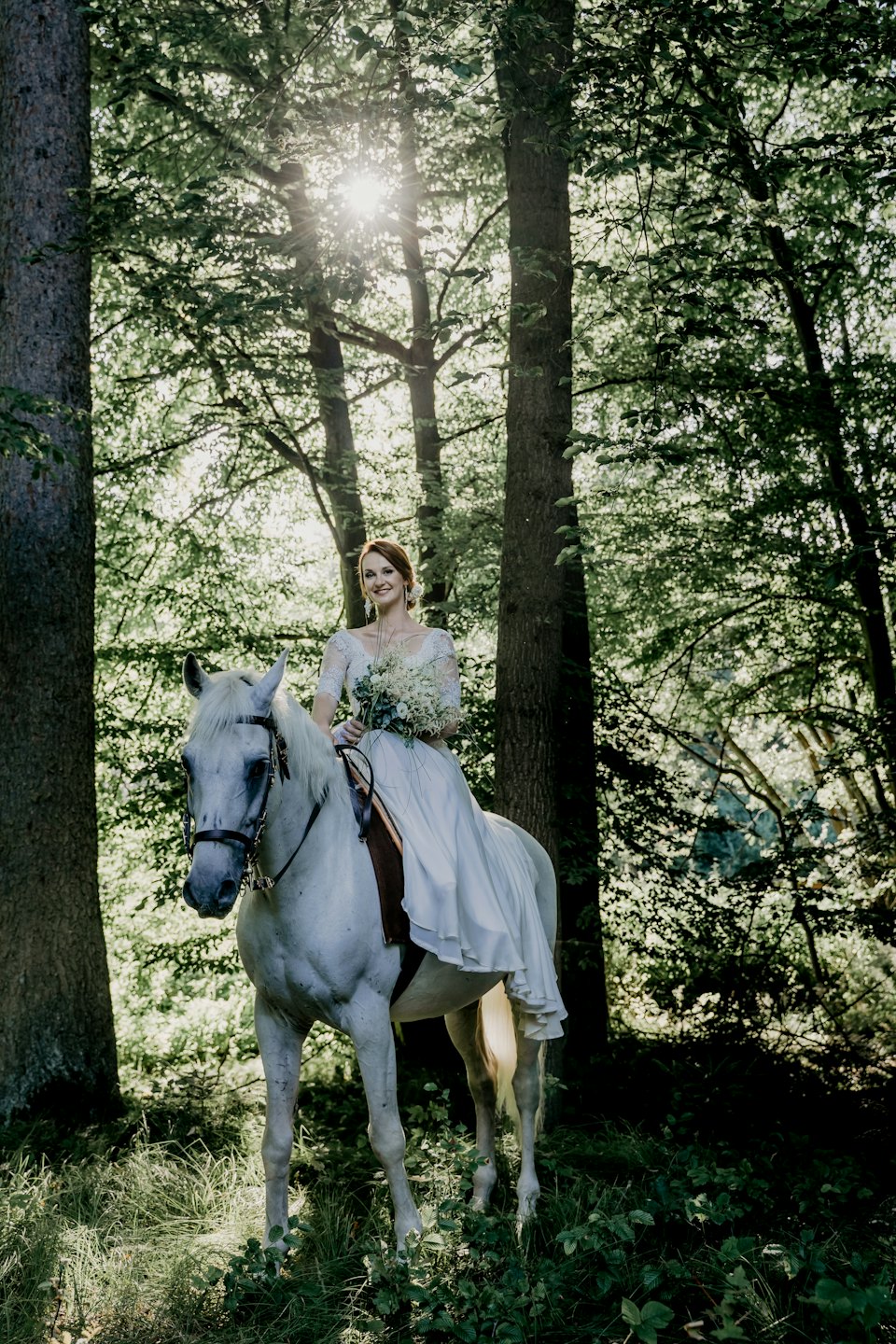 Bride in wedding dress on a horse in a forest.