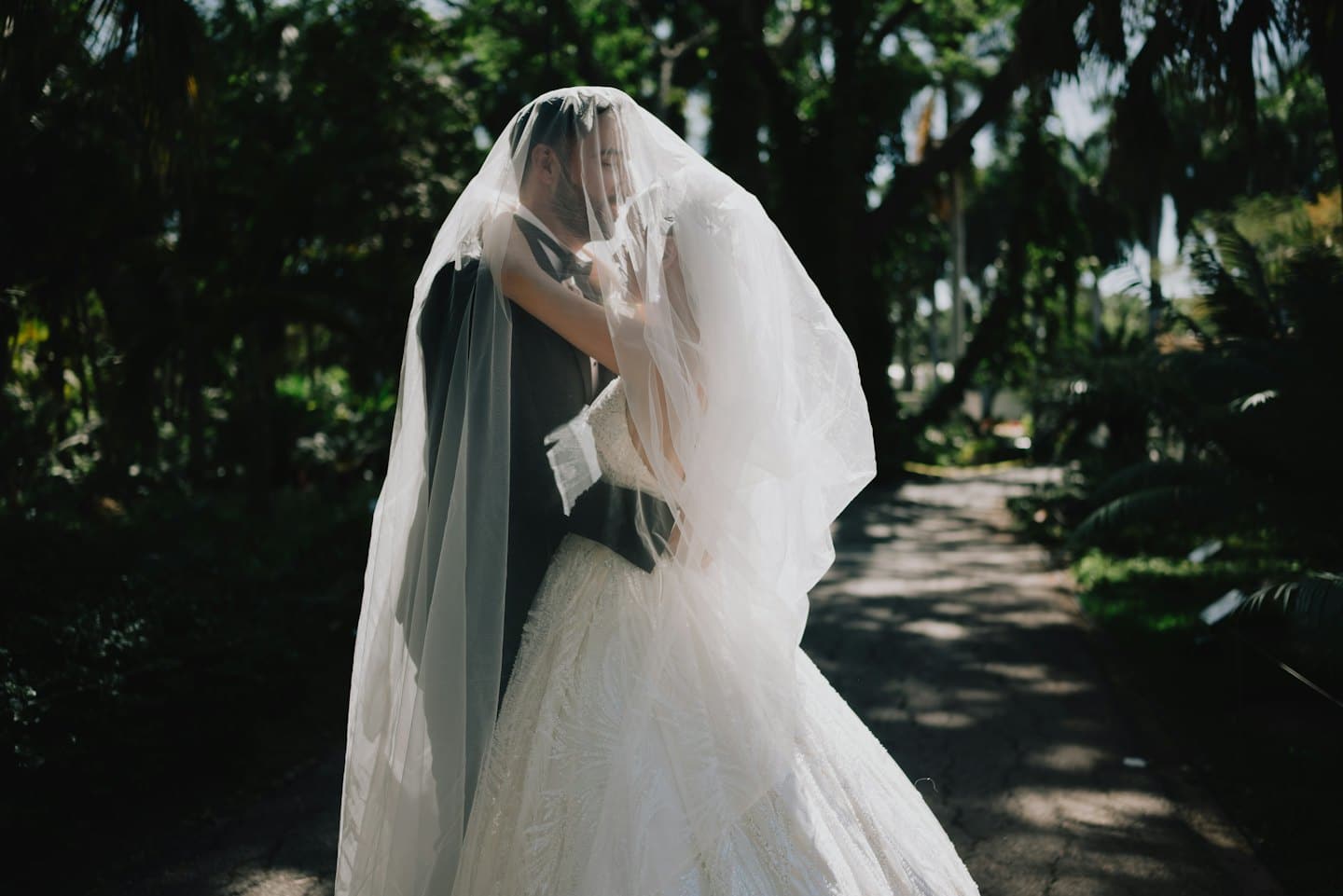 A bride and groom embrace under a sheer wedding veil.